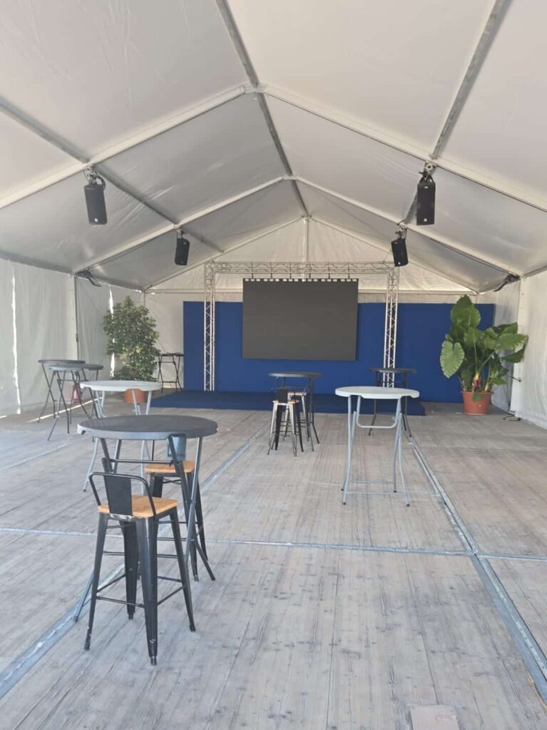 Installation événementielle sous tente avec écran, sonorisation et mobilier